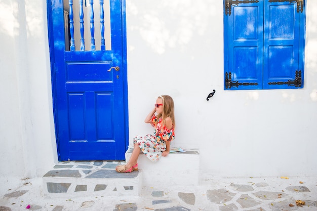Bambina all'aperto in vecchie strade un mykonos. scherzi alla via del villaggio tradizionale greco tipico con le pareti bianche e le porte variopinte sull'isola di mykonos, in grecia Foto Premium