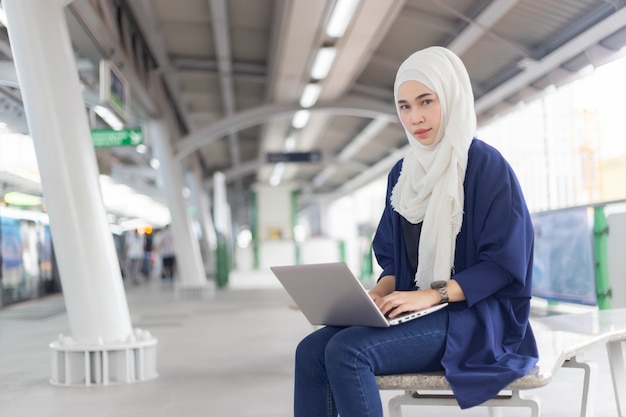 Bella giovane ragazza asiatica che lavora ad uno skytrain con un computer portatile. donne musulmane Foto Premium