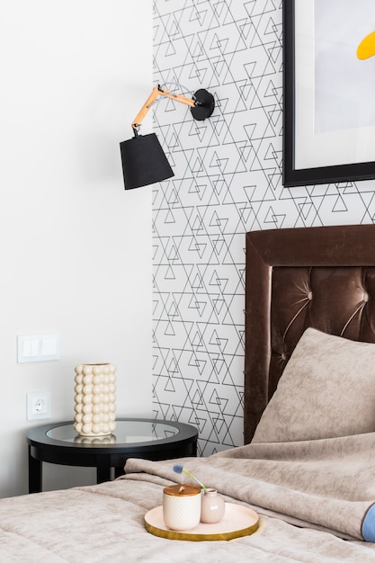 Bellissimo interno della camera da letto. letto comodo costoso con una testiera alta, arredamento su un tavolino. sulla lampada da parete e cornice per l'immagine Foto Premium
