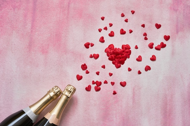 Bottiglie di champagne e cuori rossi su sfondo rosa. Foto Premium