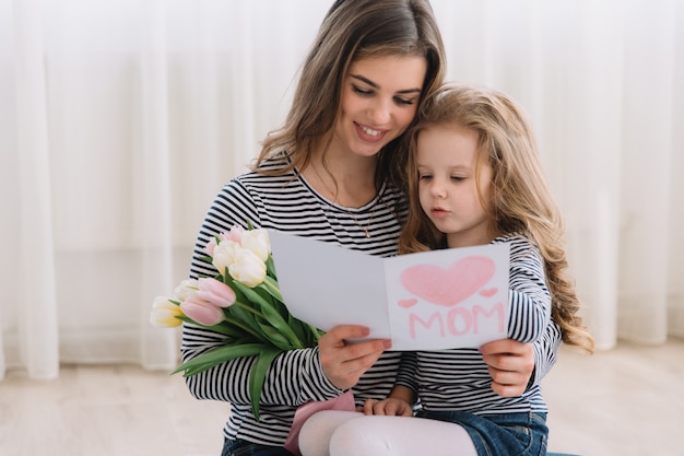 Buona festa della mamma. la figlia del bambino si congratula con le mamme e le dà una cartolina e tulipani dei fiori. Foto Premium