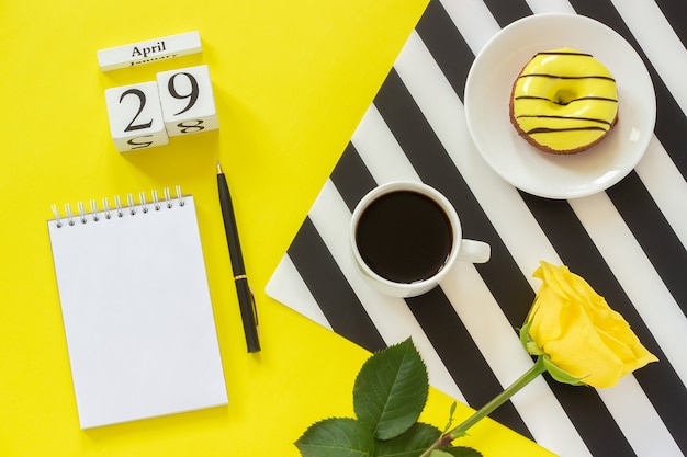 Calendario 29 aprile. tazza di caffè, ciambella e rosa, blocco note per il testo. luogo di lavoro elegante Foto Premium
