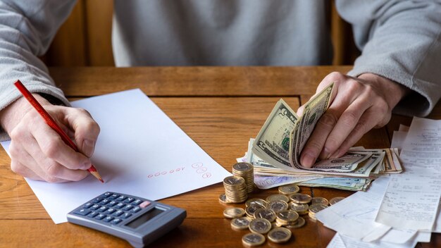 Chiuda sull'uomo con il conteggio del calcolatore, prendendo le note a casa, la mano è scrive in un taccuino. monete impilate sistemate a deesk. concetto di finanze di risparmio. Foto Premium