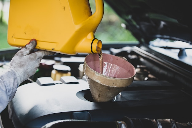 Chiuda sulla mano del meccanico automatico che versa e che sostituisce l'olio fresco nel motore di automobile al garage di riparazione automatica. manutenzione dell'automobile e concetto di industria Foto Gratuite