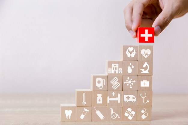 Concetto di assicurazione sanitaria, mano che organizza il blocco di legno che impila con l'assistenza sanitaria dell'icona medica, per salute Foto Premium