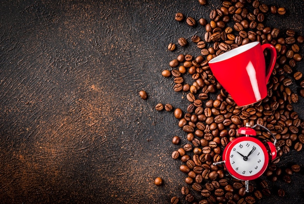 Concetto di un allegro, buon inizio di giornata, caffè mattutino. sfondo arrugginito scuro con chicchi di caffè, una sveglia e una tazza di caffè. vista dall'alto copia spazio Foto Premium