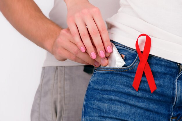Coppia in amore concetto di sesso sicuro. uomo maschio del tipo che ottiene preservativo dalla tasca dei jeans della donna femminile della ragazza con il nastro rosso appuntato come simbolo degli aiuti Foto Premium