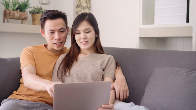 Coppie asiatiche facendo uso del computer portatile per il web di ricerca in salone a casa Foto Gratuite