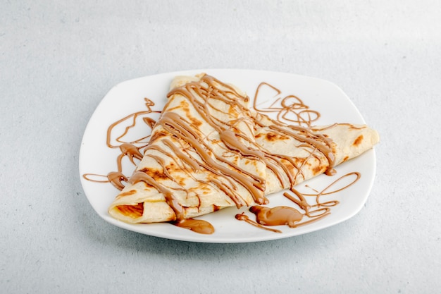 Crepe con sciroppo di cacao al cioccolato in un piatto bianco in uno sfondo bianco. Foto Gratuite