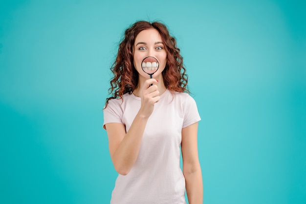 Donna attraente con capelli ricci che mostra i denti attraverso la lente di ingrandimento Foto Premium
