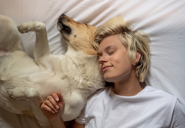 Donna bionda felice che si situa a letto con il suo cane da pastore Foto Premium