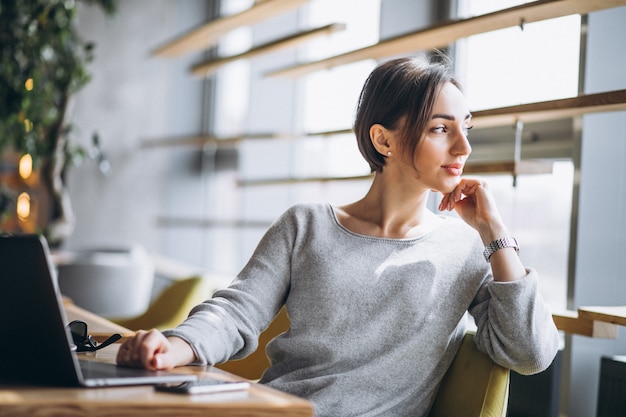 Donna che si siede in un caffè bevendo caffè e lavorando su un computer Foto Gratuite