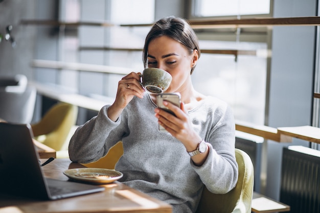 Donna che si siede in un caffè bevendo caffè e lavorando su un computer Foto Gratuite