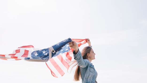 Donna che sorride e che tiene ampia bandiera americana d'ondeggiamento su in cielo Foto Gratuite