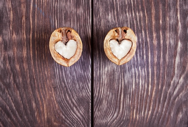 Due metà della noce a forma di cuore giacciono su due parti del tavolo di legno dipinto di scuro Foto Premium