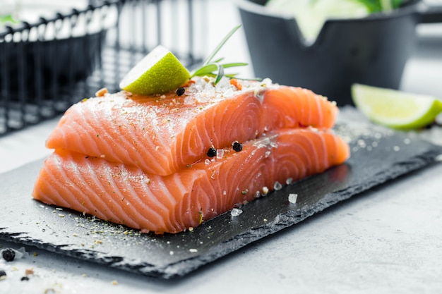 Due pezzi di filetto di salmone crudo con erbe fresche rosmarino, spezie e olio d'oliva su lastra di ardesia nera Foto Premium