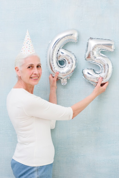 Elder bella donna che tiene il numero di palloncino stagnola sul suo compleanno Foto Gratuite