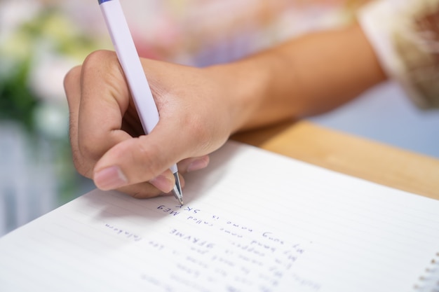 Equipaggi lo studente che prende e che scrive le note sul taccuino con la penna in biblioteca all'università dell'istituto per i compiti Foto Premium