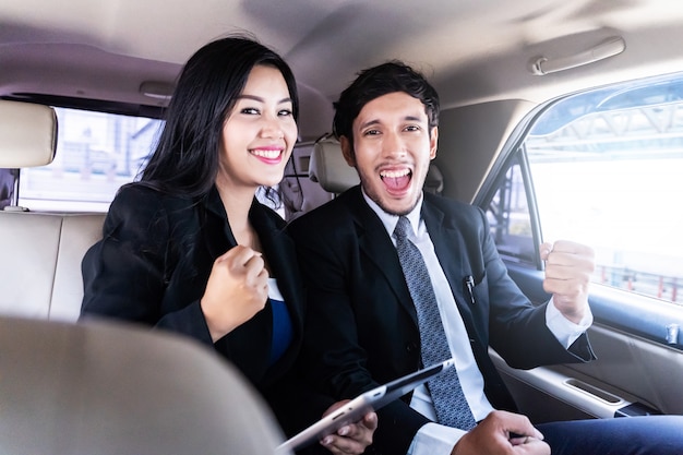 Felice uomo d'affari bello e donna d'affari seduto in auto di lusso limousine, lavorando su computer portatile, funziona sempre e ovunque concetto. Foto Premium