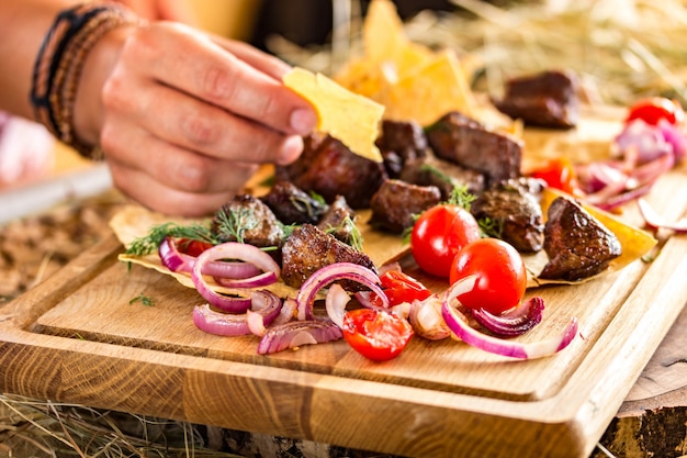 Fette di carne fritta con cipolle e pomodorini su una sottile torta piatta. la mano femminile prende un pezzo di torta. colori orizzontali e luminosi, spazio per il testo Foto Premium