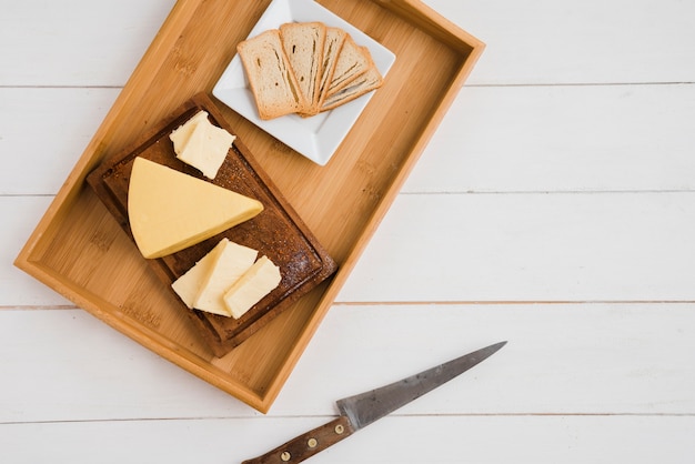 Fette di pane e spicchi di formaggio sul vassoio in legno con coltello Foto Gratuite