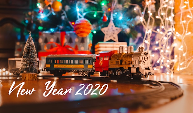 Giochi la locomotiva a vapore d'annata sul pavimento sotto un albero di natale decorato su un fondo della ghirlanda delle luci del bokeh. Foto Premium