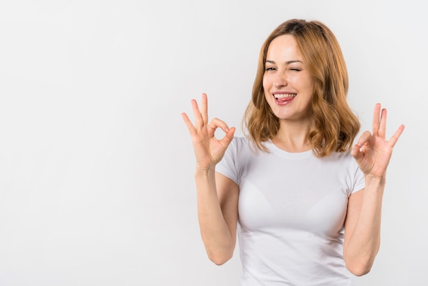 Giovane donna che morde la sua lingua che mostra gesto giusto con due mani che sbatte le palpebre Foto Gratuite