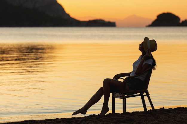 Giovane donna che si siede sul sedile sul tramonto sulla riva di un lago Foto Gratuite