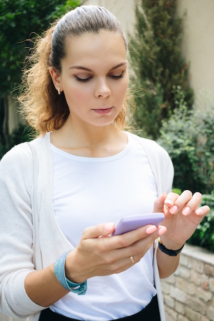 Giovane donna in abiti d'affari, camminando per la strada e utilizzando un telefono cellulare con touch screen Foto Premium