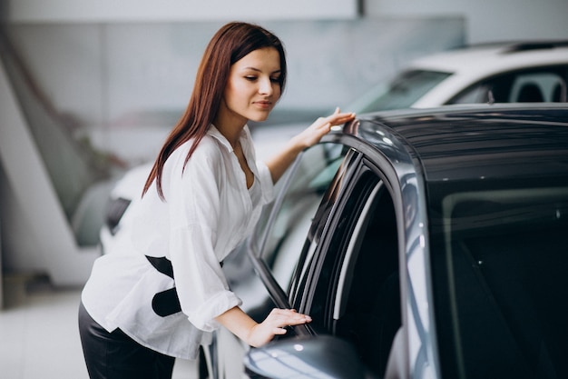 Giovane donna in una sala d'esposizione dell'automobile che sceglie un'automobile Foto Gratuite