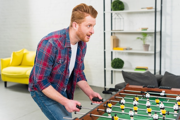 Giovane emozionante che gioca il gioco di calcio della tavola di calcio nel salone Foto Gratuite
