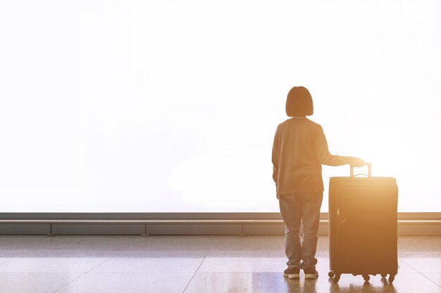 Giovane turista con bagagli che stanno davanti al grande tabellone per le affissioni della luce bianca all'aeroporto Foto Premium