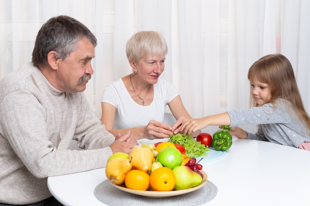 I nonni con la nipote preparano cibo sano in cucina. famiglia che prepara un'insalata insieme Foto Premium