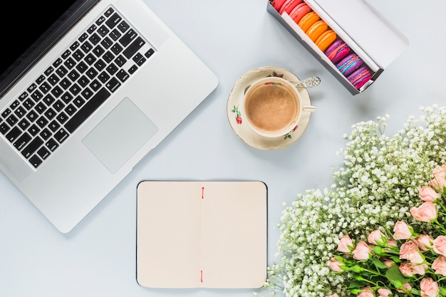 Il computer portatile; tazza di caffè; mazzo dei fiori e dei maccheroni su fondo bianco Foto Gratuite