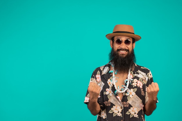 Il di un uomo felice con una lunga barba che indossa un cappello, indossa una camicia a righe che mostra un gesto su un blu. Foto Gratuite