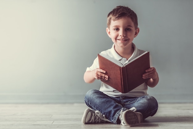 Il ragazzino sveglio sta tenendo un libro, sta esaminando la macchina fotografica. Foto Premium