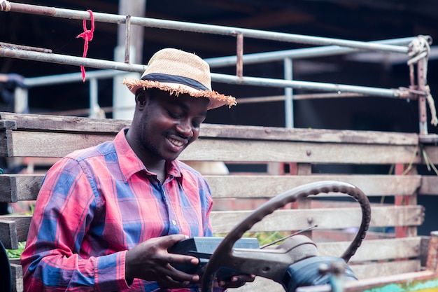 L'uomo africano dell'agricoltore con il retro ricevitore radiofonico sulla spalla sta sorridere felice all'aperto sulla vecchia automobile con fondo Foto Premium