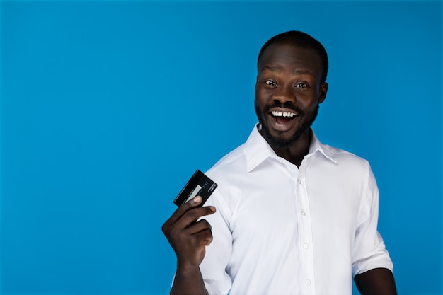 L'uomo afroamericano sorridente in avanti sorridente in camicia bianca sta tenendo la carta di credito in una mano Foto Gratuite