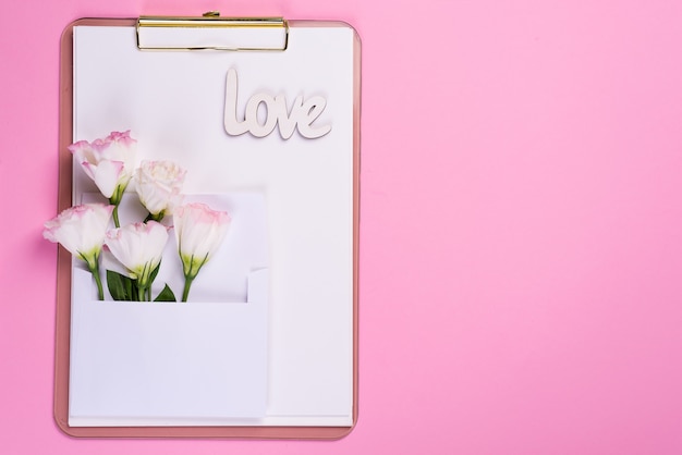 La composizione minima con un eustoma fiorisce in una busta sulla lavagna per appunti su un fondo rosa, vista superiore. cartolina d'auguri di san valentino, compleanno, madre o matrimonio Foto Premium