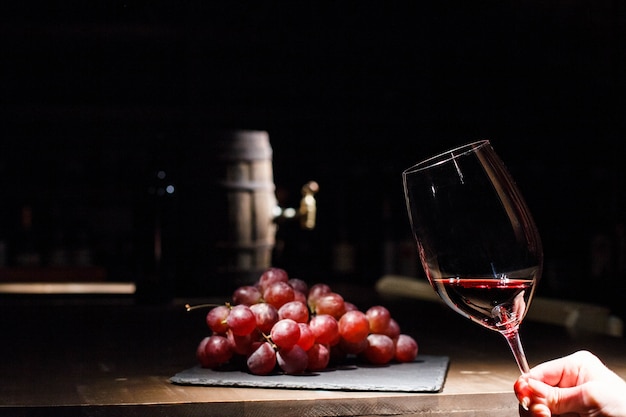 La donna tiene un bicchiere di vino prima di un grappolo d'uva che si trova sulla piastra nera Foto Gratuite