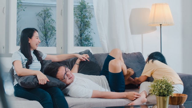 La giovane famiglia asiatica felice gioca insieme sullo strato a casa. godere cinese felice della figlia del padre e del bambino della madre che trascorre insieme il tempo in salone moderno nella sera. Foto Gratuite