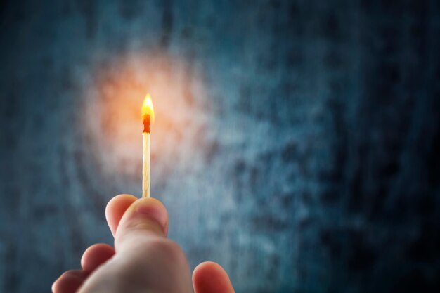 La mano tiene un fiammifero, illumina l'oscurità con la fiamma. Foto Premium
