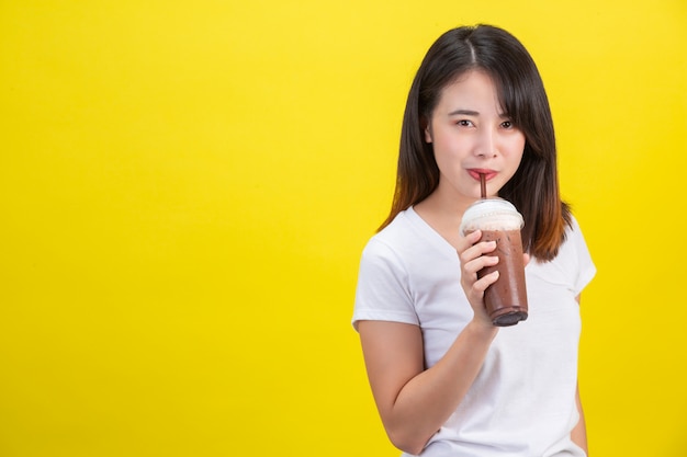 La ragazza beve acqua fredda dal cacao da un bicchiere di plastica trasparente su un giallo. Foto Gratuite