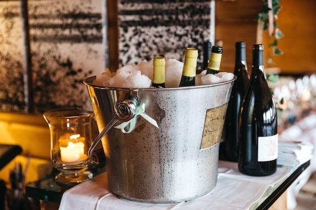 Le bottiglie con champagne si stanno raffreddando in un secchio con ghiaccio e le bottiglie con vino sono vicine Foto Gratuite