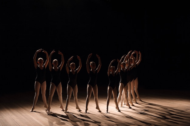 Le giovani ballerine che praticano una danza coreografica fanno piovere tutte le braccia in un grazioso unisono durante le prove in una scuola di balletto Foto Premium
