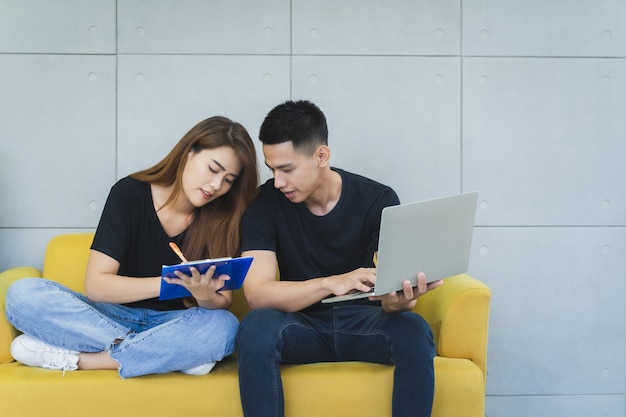 Le giovani coppie asiatiche felici del onwer della pmi di affari nell'abbigliamento casual con il fronte di smiley sta usando il computer portatile e stanno controllando il prodotto sulle azione e scrivono sui appunti al loro ministero degli interni startup, venditore di consegna Foto Premium