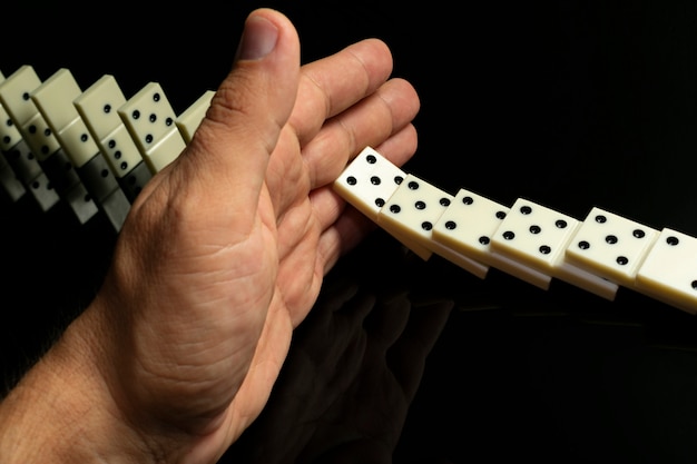 Le nocche di domino che cadono in fila una dopo l'altra vengono fermate a mano, su un tavolo di vetro nero Foto Premium