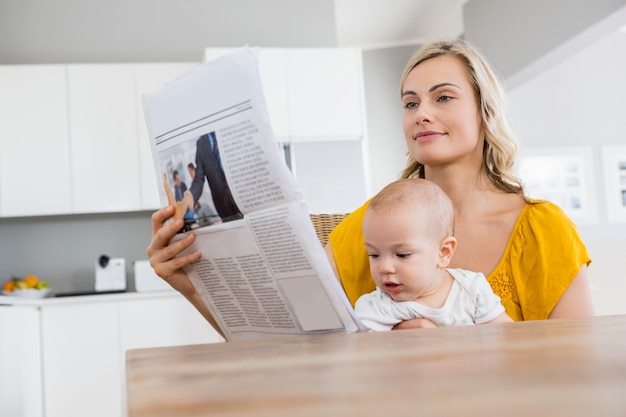 Madre che legge il giornale con il neonato in cucina Foto Gratuite