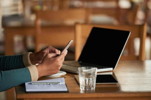 Mani dell'uomo irriconoscibile che utilizza smartphone nel caffè e computer portatile sulla tavola Foto Gratuite