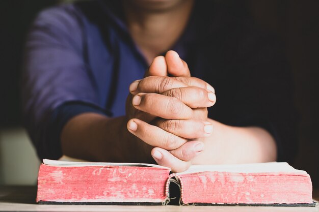 Mani giunte in preghiera su una sacra bibbia in concetto di chiesa per ...